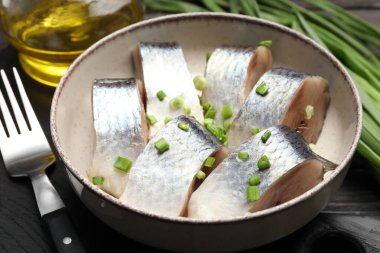 Siyah ahşap masada servis edilen taze soğanlı lezzetli ringa balıkları.