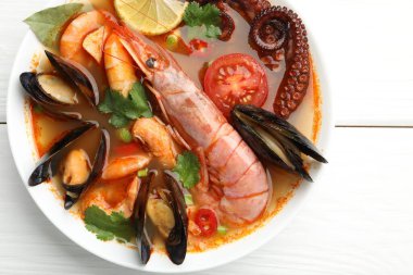 Lezzetli deniz ürünleri çorbası, beyaz ahşap masada, üst manzara.