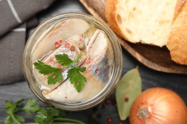 Kavanozda baharat ve siyah masada ekmek olan lezzetli ringa balıkları.