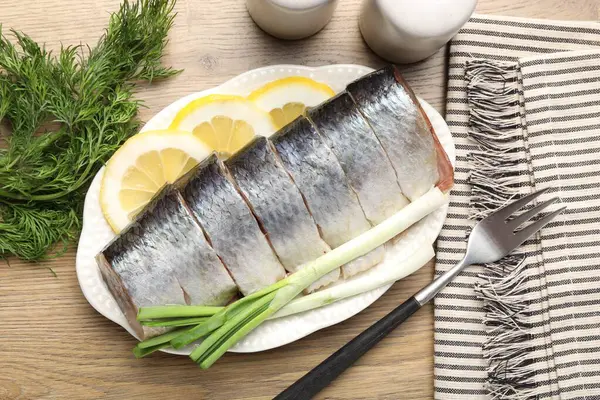 Limon dilimli lezzetli ringa balıkları, yeşil soğan ve ahşap masa üzerinde dereotlar.