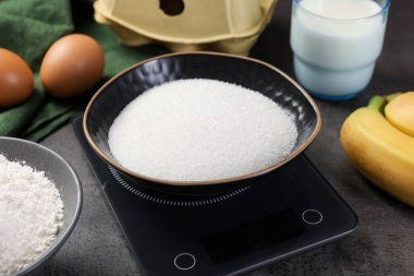 Gri masadaki şeker ve diğer ürünlerle birlikte dijital mutfak terazisi, yakın plan.