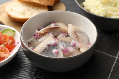 Siyah ahşap masada servis edilen soğanlı lezzetli ringa balıkları, yakın plan.