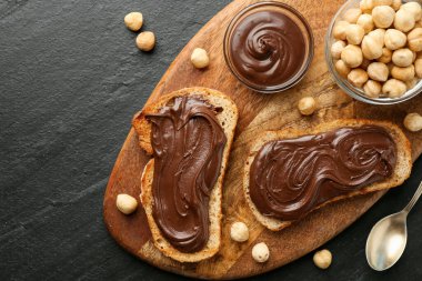 Çikolata sürülmüş ekmek dilimleri ve koyu dokulu masada fındıklar, düz uzanmış.