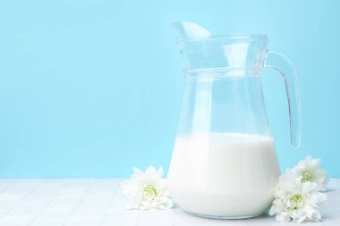 Açık mavi arka planda beyaz masada taze süt ve çiçekler. Metin için boşluk