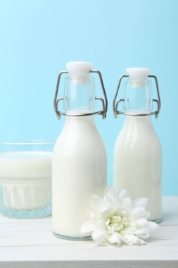 Açık mavi arka planda beyaz masada taze süt ve çiçek