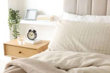 Alarmlı komodinli komodin, bir bardak su ve yatağın yanında kitap.