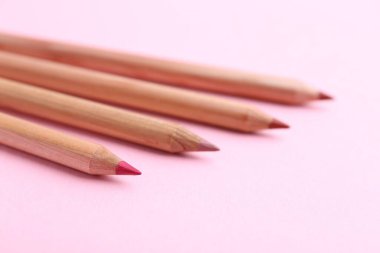 Açık pembe arka planda birçok farklı dudak kalemi, yakın plan.