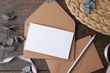 Boş tebrik kartı, kağıt zarflar, okaliptüs yaprakları, tahta masa üzerinde kurşun kalem ve kurdele.