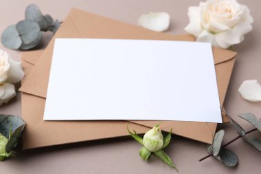 Boş tebrik kartı, kağıt zarflar, gül çiçekleri ve bej arka planda okaliptüs dalları, yakın plan.