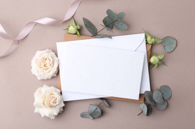 Boş tebrik kartı, kağıt zarflar, gül çiçekleri, okaliptüs dalları ve bej arka planda kurdele, düz uzanma