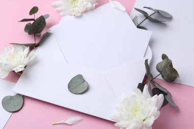 Kağıt zarftaki boş tebrik kartı, kasımpatı çiçekleri ve pembe arkaplanda okaliptüs dalları, yakın plan.