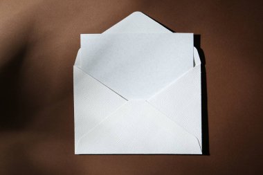 Kahverengi arkaplandaki kağıt zarfın içindeki boş tebrik kartı, üst görünüm