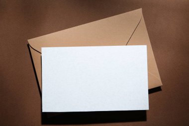 Kahverengi arkaplanda boş tebrik kartı ve kağıt zarf, üst görünüm