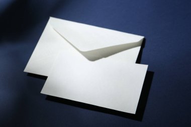 Koyu mavi arkaplanda boş tebrik kartı ve kağıt zarf, yakın plan