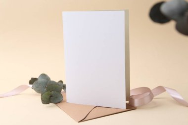 Boş tebrik kartı, zarf, okaliptüs yaprakları ve bej arka planda kurdele, yakın plan.