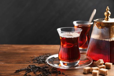 Geleneksel Türk çayı cam fincanlar, çaydanlık, kuru yapraklar ve ahşap masa üzerinde esmer şeker, yakın plan. Metin için boşluk