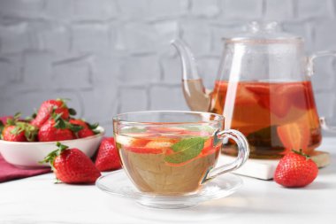 Aromatik meyve çayı, çilek ve nane şekeri beyaz masada, yakın plan.