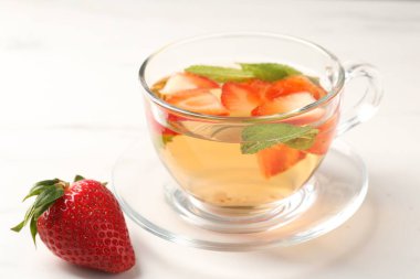 Aromatik meyve çayı, çilekli ve nane şekerli beyaz mermer masada, yakın plan.