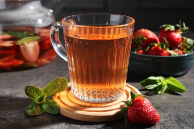 Aromatik meyve çayı, çilek ve nane şekeri gri masada, yakın plan.