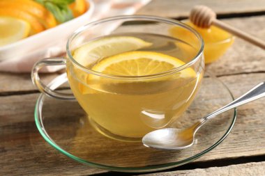 Cam fincanda aromatik meyve çayı, portakal, limon ve bal ahşap masada, yakın plan.