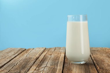 Açık mavi arka planda, cam bardakta, tahta masada taze süt, yakın plan. Metin için boşluk