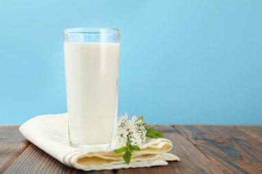 Bardaktaki taze süt ve ahşap masadaki çiçekler açık mavi arka planda, yakın plan. Metin için boşluk