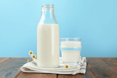 Taze süt ve çiçekler ahşap masada açık mavi arka planda, yakın plan