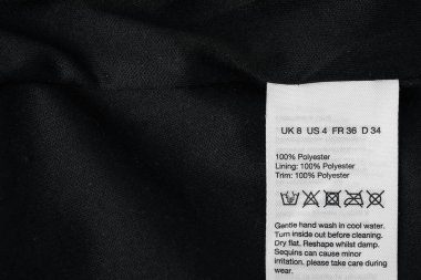 Üzerinde özen sembolleri ve siyah giysi içeriği olan kıyafet etiketi, üst görünüm. Metin için boşluk