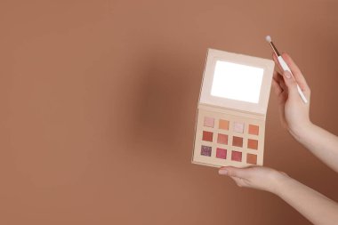 Göz farı paleti olan ve bej arka planda fırçası olan bir kadın, yakın plan. Metin için boşluk