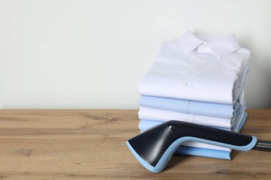 Düz vapur ve beyaz duvarın yanındaki ahşap masada katlanmış gömlek yığını.