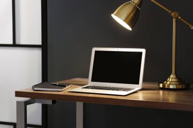 Home office. Comfortable workplace with laptop and lamp on wooden desk indoors