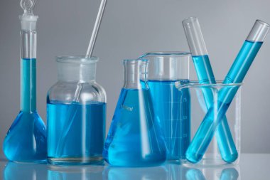 Aynanın yüzeyinde gri arka planda mavi sıvı bulunan laboratuvar camları