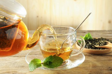 Çaydanlıktan cam fincana taze demlenmiş çay dökülüyor ahşap masada, yakın plan.