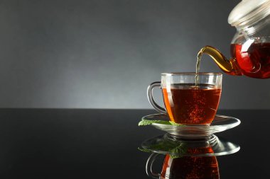 Koyu ayna masasında çaydanlıktan fincana taze demlenmiş çay doldurmak, yakın plan. Metin için boşluk