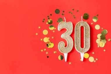 30th birthday. Number shaped candles and confetti on red background, flat lay. Space for text