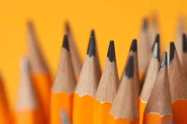 Many graphite pencils on orange background, closeup