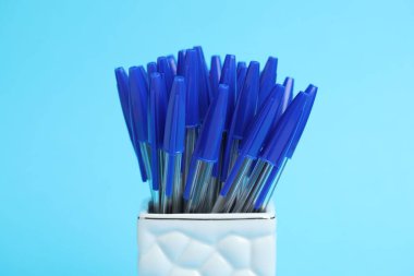 Many ballpoint pens in holder on light blue background, closeup