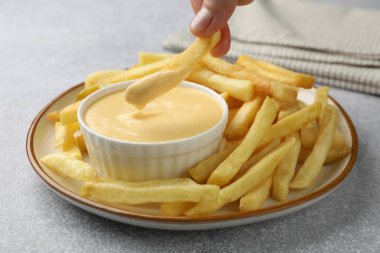 Gri masada patates kızartmasını peynir sosuna batıran kadın, yakın plan.