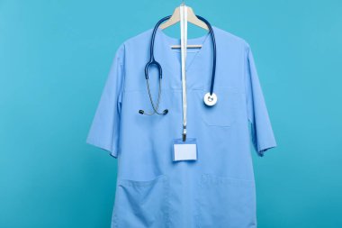 Steteskop ve rozetli sağlık çalışanı üniforması mavi arka planda.