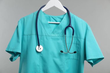 Steteskoplu sağlık çalışanı üniforması gri arka planda, yakın plan.
