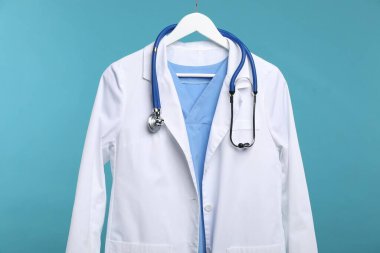 Mavi arka planda asılı steteskoplu doktor ceketi.
