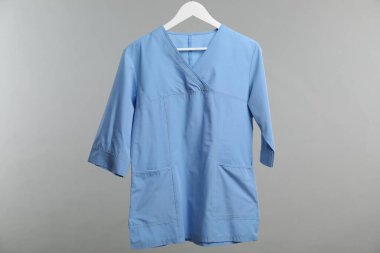 Sağlık çalışanı üniforması gri arkaplanda asılı.