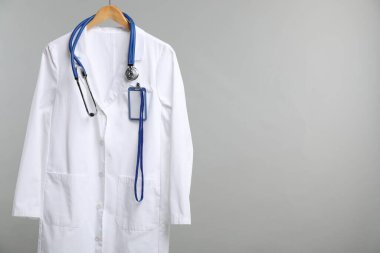 Üzerinde steteskop ve rozet olan doktor ceketi gri arka planda. Metin için boşluk