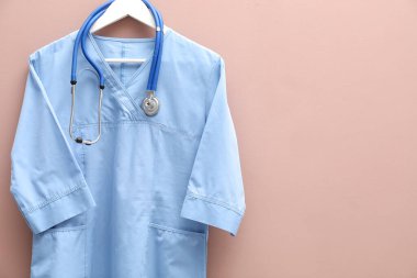 Bej arka planda steteskop takılı sağlık çalışanı üniforması. Metin için boşluk