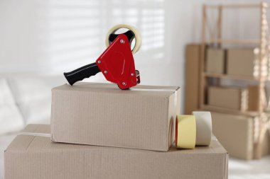 Kapalı alandaki karton kutunun üzerinde yapışkan bant ruloları olan bir dağıtıcı.