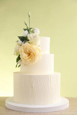 Ahşap masada çiçeklerle süslenmiş nefis bir düğün pastası açık yeşil arka planda, yakın plan.