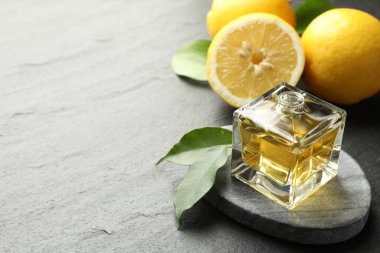 Açık parfüm şişesi aromatik esanslı yağ, koyu dokulu masa üzerinde yapraklar ve limonlar, yakın çekim. Metin için boşluk