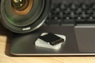 SD hafıza kartı, tutucu, fotoğraf makinesi ve laptop ahşap masada, yakın plan.