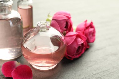 Gri desenli masa üzerinde aromatik esanslı yağlar ve güllerle parfüm şişelerini aç, yakın plan.