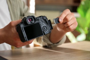 SD hafıza kartını ahşap masadaki fotoğraf makinesine yerleştiren adam, yakın plan.